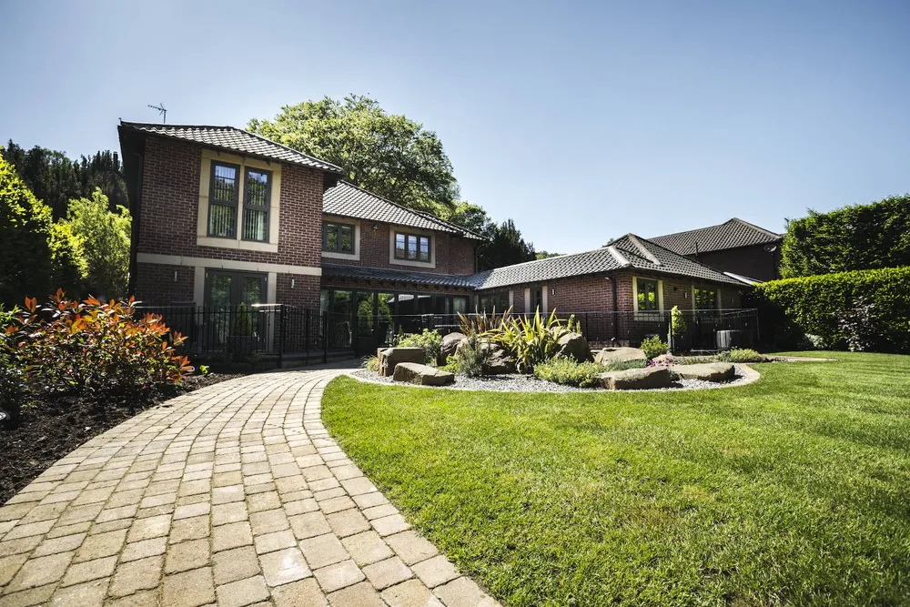 Two-story brick house with large windows, a curved stone pathway, and a neatly landscaped front yard.